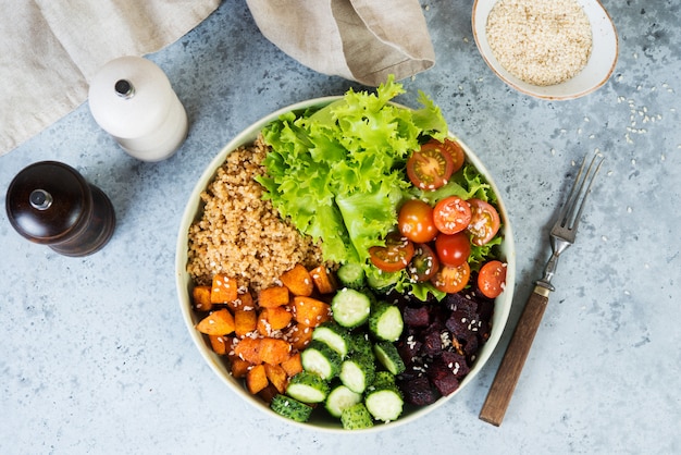 Vegetarian dish a bowl of healthy quinoa with fresh and baked vegetables on a gray concrete background.