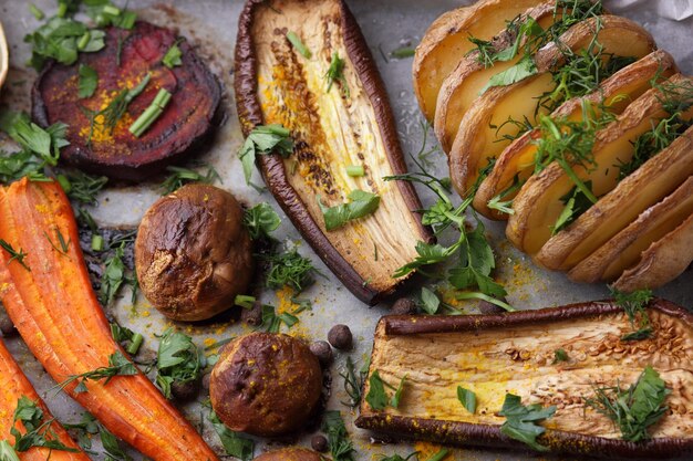 Vegetarian food closeup Baked slices of eggplant beets carrots onions potatoes whole mushrooms spices and herbs on parchment paper