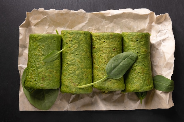 Vegetarian green pancake rolls breakfast. Spinach pancake rolls and spinach leaves on dark wooden desk. Copy space.