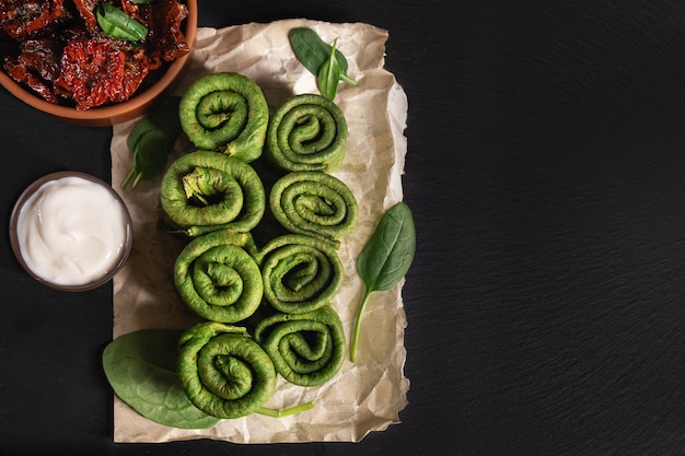 Vegetarian green pancake rolls and dried tomato breakfast. Spinach pancake rolls with dried tomatoes on dark wooden desk.