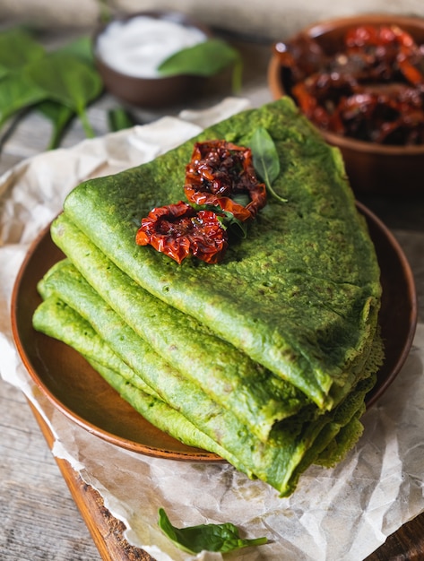 Vegetarian green pancakes decorated with dried tomatoes. Spinach pancakes in a brown plate on wooden desk.