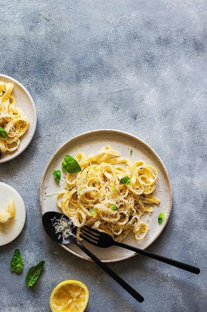 Vegetarian pasta  with lemon, basil, parmesan and black pepper searved on a gray stone background. Flatlay with copy space.