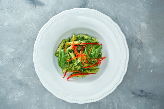 Vegetarian pasta with spinach and pepper in a white plate on a gray background