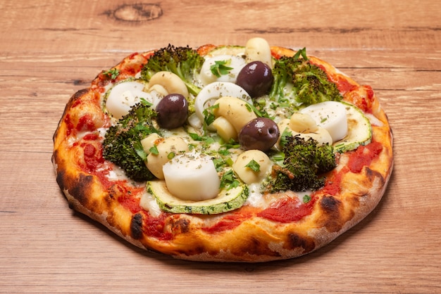 Vegetarian pizza, with broccoli, hearts of palm, olives and zucchini, served on a rustic wooden table.