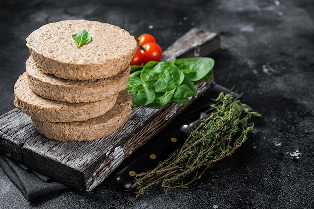 Vegetarian plant based meat burger patties raw vegan cutlets on wooden board with herbs Black background Top view Copy space