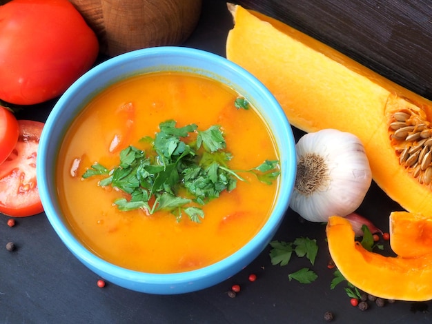 Vegetarian pumpkin soup in a blue bowl Fresh tomatoes garlic pumpkin pieces