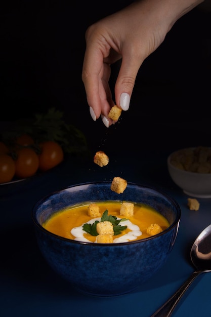 Vegetarian pumpkin soup Seasonal autumn food Spicy pumpkin soup with croutons Woman's hand throws croutons into the soup