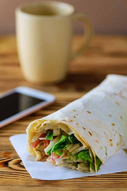 Vegetarian roll of pita bread, vegetables and greens on a wooden table.