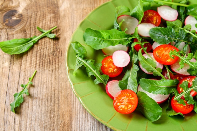 Vegetarian salad of arugula, tomato, radish and mozzarella cheese on an old wooden table.