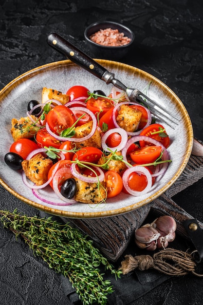 Vegetarian salad Panzanella with tomatoes, onion and bread Croutons. Black background. Top view.