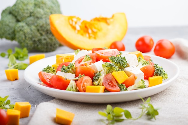 Vegetarian salad with broccoli, tomatoes, feta cheese, and pumpkin on white ceramic plate 