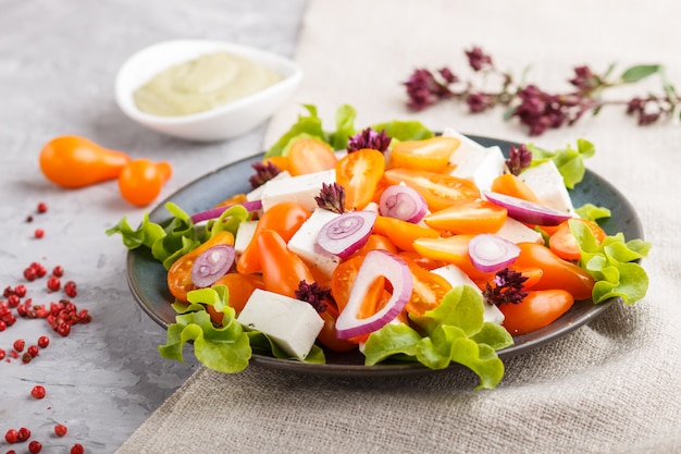 Vegetarian salad with fresh grape tomatoes, feta cheese, lettuce and onion, top view.