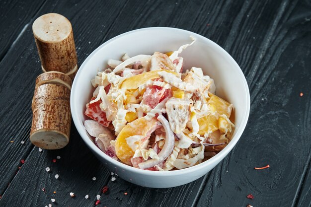 Vegetarian salad with onions, cabbage, bell peppers and tomatoes in a white bowl on a black wooden surface. Close up. Copy space