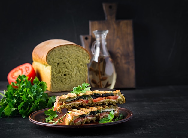 Vegetarian sandwich panini with spinach leaves, tomatoes and cheese on a dark table. Toast with cheese.