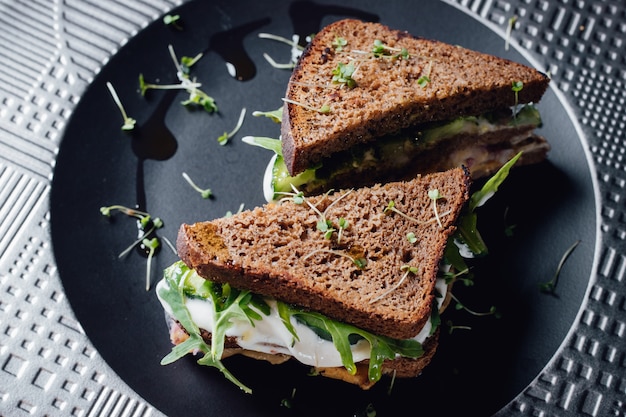 Vegetarian sandwich with whole grain bread, cucumber, egg whites, radishes and pea shoots on plate. isolated on black background, close up, top view