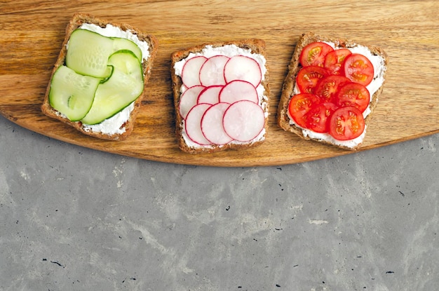 Vegetarian sandwiches with cream cheese fresh cucumber radish tomatoes on a cutting wooden board