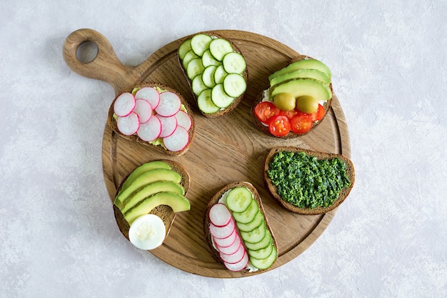 Vegetarian sandwiches on the wood board on the gray background.  Delicious breakfast. Flat lay, top view.