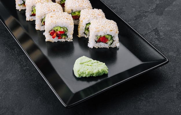 Vegetarian sushi maki rolls with sesame seeds on black plate