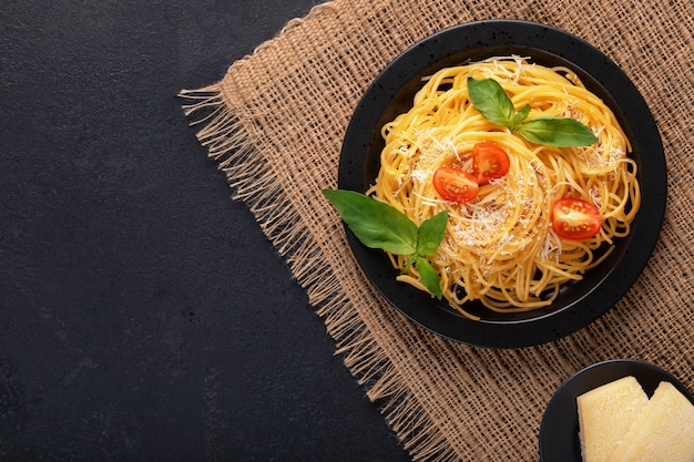 Vegetarian vegetable appetizing classic Italian spaghetti pasta with basil, tomato and  parmesan on black plate on a dark table. Top view, horizontal.