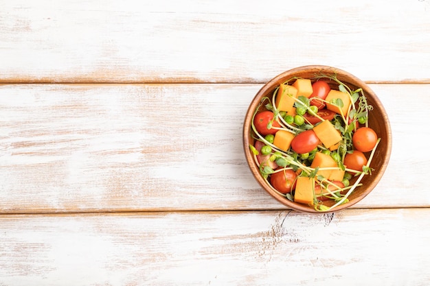 Vegetarian vegetable salad of tomatoes pumpkin microgreen pea sprouts on white wooden background Top view copy space