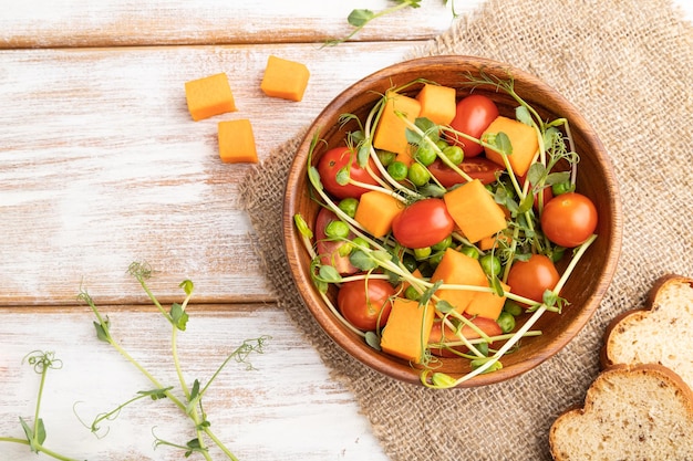 Vegetarian vegetable salad of tomatoes pumpkin microgreen pea sprouts on white wooden background Top view