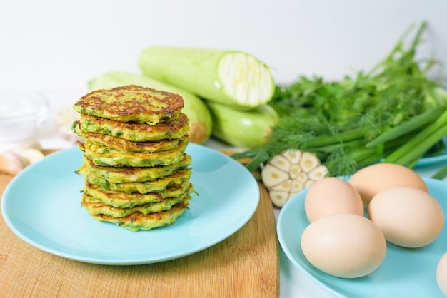 Veggie fried pancakes with zucchini and greens on a blue plate on a light background on a wooden Board. top view, selective focus, space for text