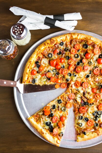 Veggie pizza with olives and cherry tomatoes on the table.