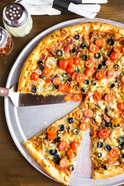 Veggie pizza with olives and cherry tomatoes on the table.