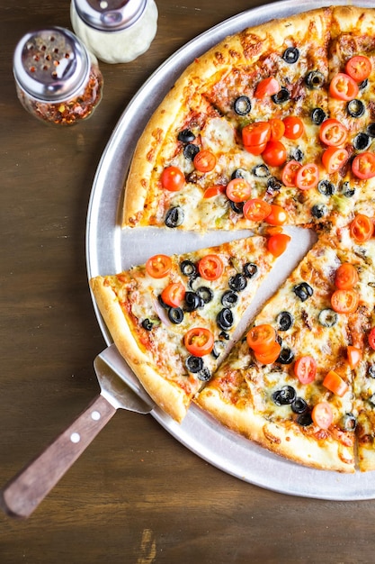 Veggie pizza with olives and cherry tomatoes on the table.