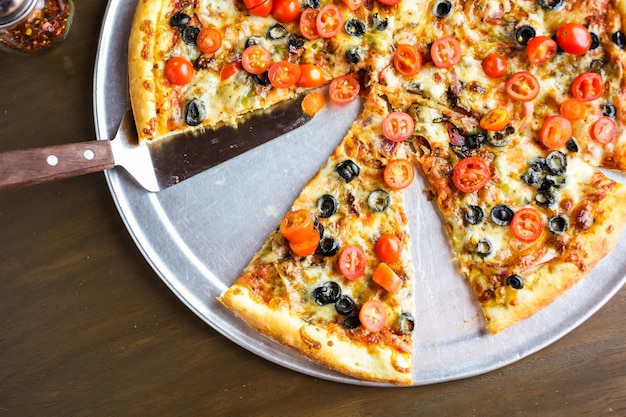 Veggie pizza with olives and cherry tomatoes on the table.