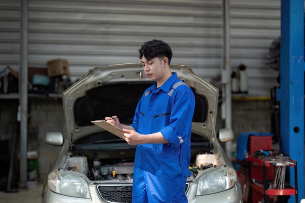 Vehicle service maintenance asian man checking under car condition in garage Automotive mechanic maintenance checklist document Car repair service concept