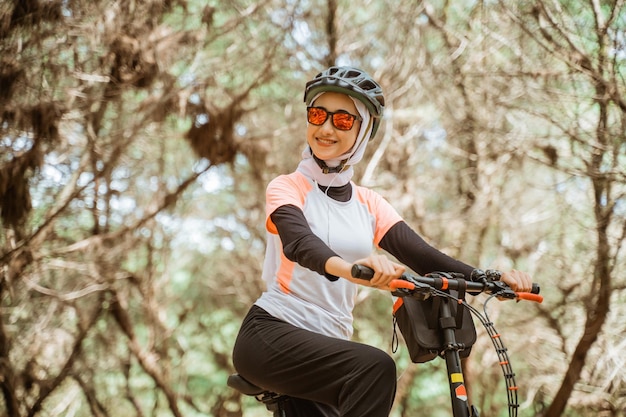 Veiled girl in sunglasses smiling while riding bicycle in park