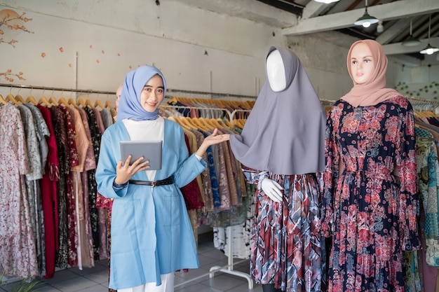 A veiled woman a tablet while holding a headscarf mannequin