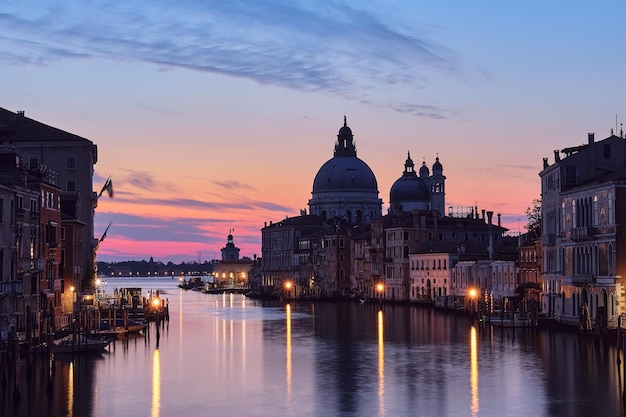 Venice at night. Cityscape image of Grand Canal in Venice, with Santa Maria della Salute Basilica reflected in calm sea. Lights of passenger boat on the water.