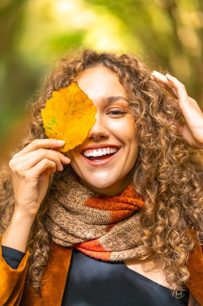 Photo vertical autumn portrait of a smiling woman with curly hair hiding on a leaf