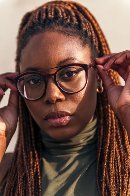 Vertical close-up portrait of a young black woman putting on her glasses and looking at the camera, concept of youth and racial diversity