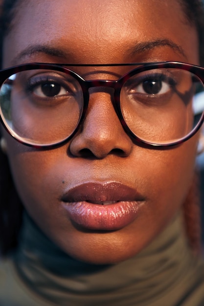 Vertical closeup portrait of a serious young black woman with glasses looking at the camera