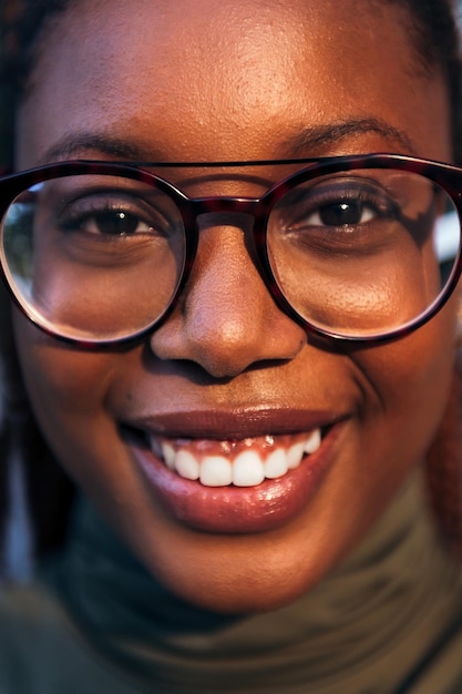 Vertical closeup portrait of a young black woman with glasses smiling looking at the camera