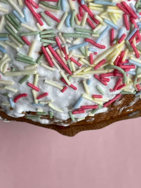 Vertical cropped close up of glazed paska easter cake with colorful sprinkles pink background