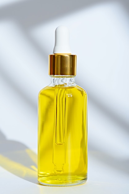 Vertical dropper glass bottle with yellow cosmetic oil on white background