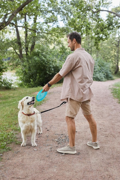 Vertical full length portrait of smiling man playing with dog outdoors in summer at green park