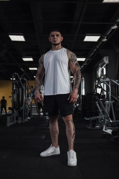 Vertical full length shot of a big muscular tattooed sportsman standing in the gym