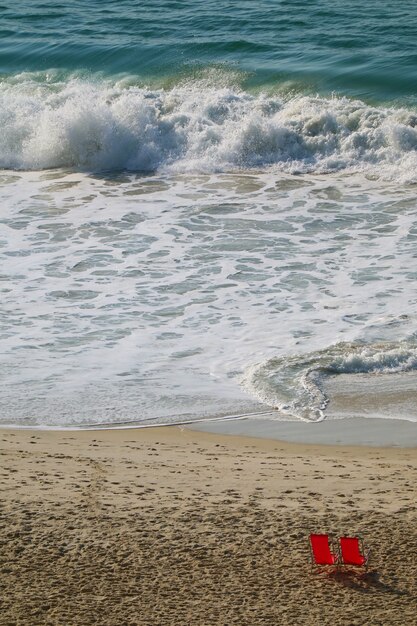 Vertical image of the crashing waves in the ocean with red beach chairs on the sandy beach