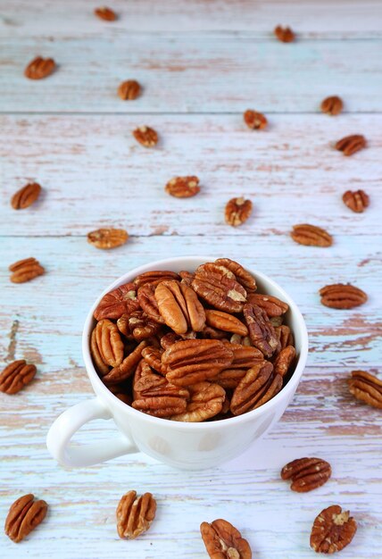 Vertical Image of a Cup Full of Pecan Nuts with Some Scattered on Wooden Table