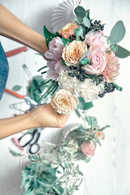 Photo vertical image of female florist at work. arranging various flowers in bouquet. top view. a teacher of floristry in master classes or courses. professional, floral concept. copy space for design