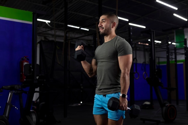 Vertical image of a latin athlete doing bicep exercises with two dumbbells in a gym