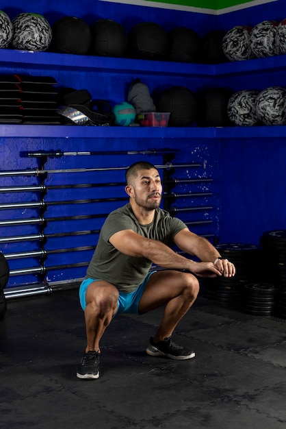 Vertical image of a latin man doing squats wearing sportswear in a crossfit gym