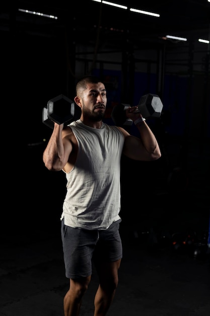 Vertical image of a muscular man pressing with a pair of dumbbells in the gym