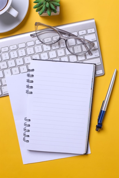 Vertical image of office desk with wireless keyboard pen notebook glasses and succulent with blan