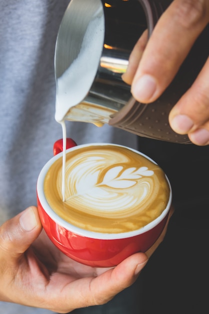 Vertical image of pouring milk to espresso coffee make latte art on red cup coffee